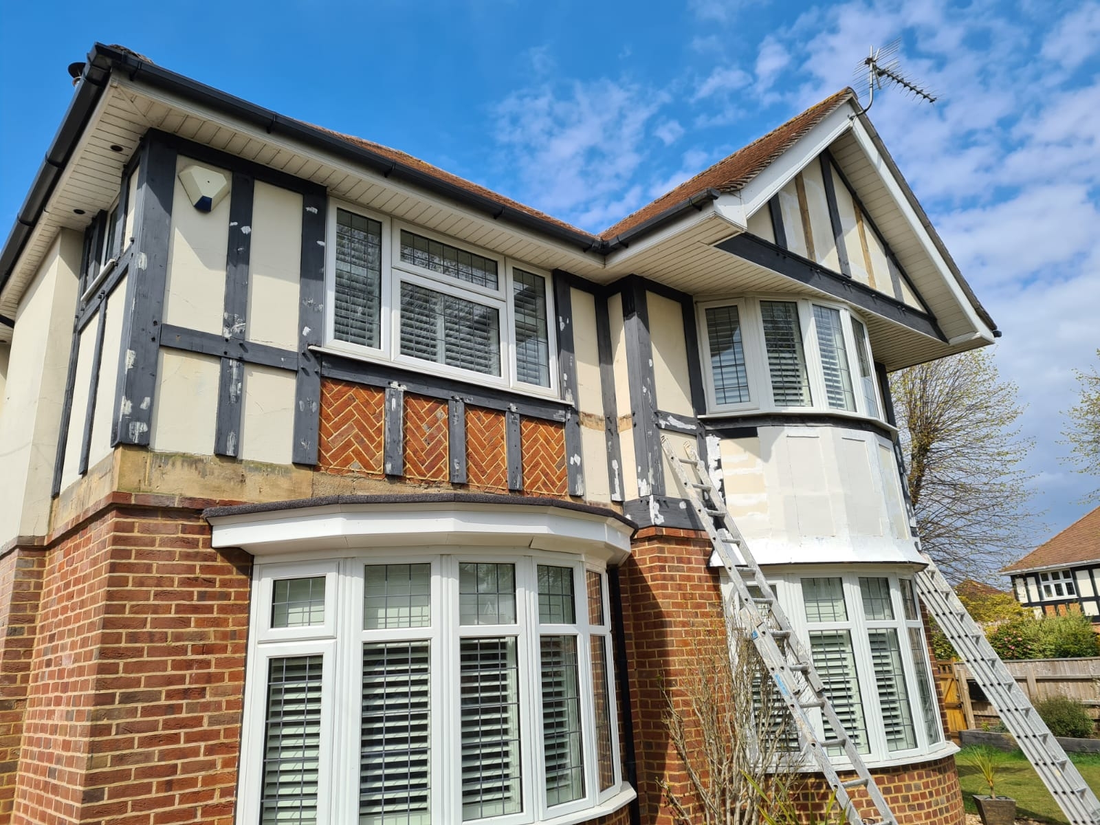 Mock-Tudor house front mid-repaint with ladders up