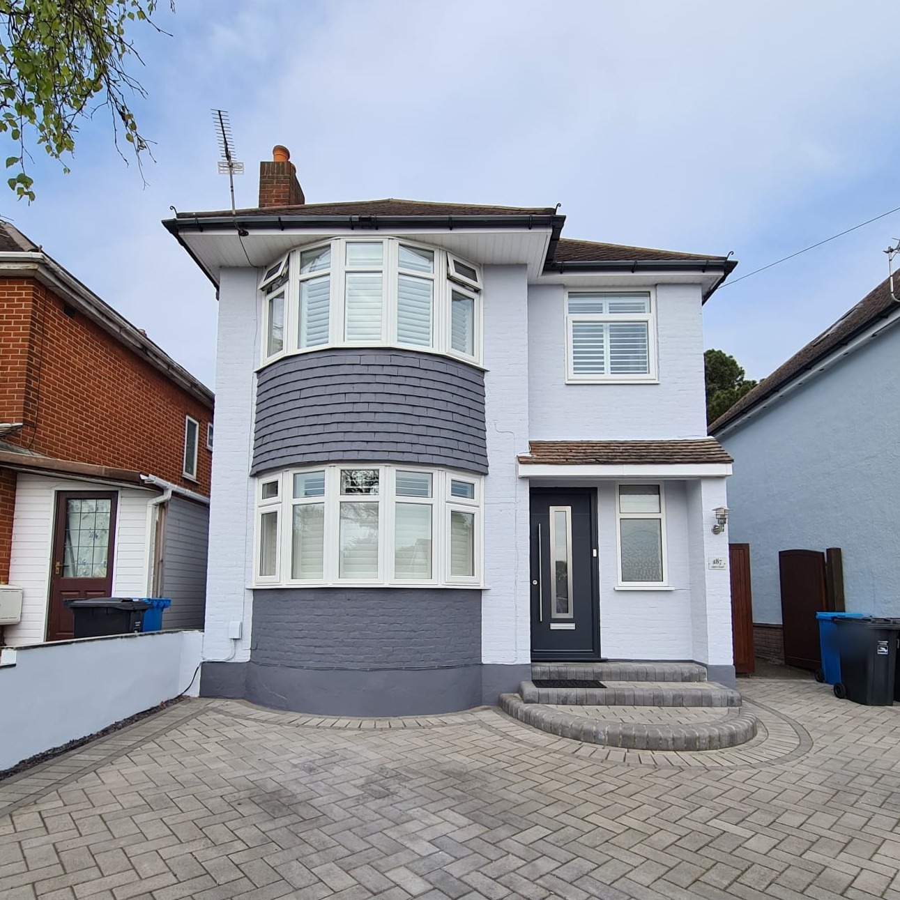 Detached house freshly painted white with a grey slate-hung bay
