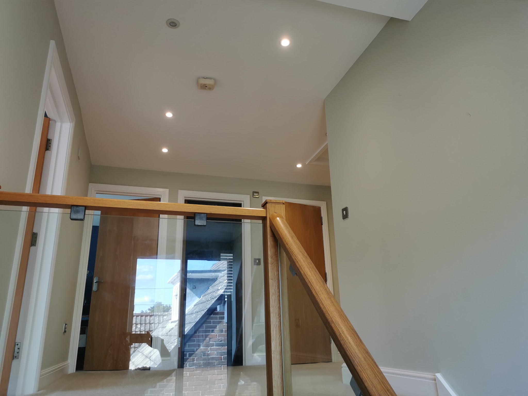 Sage green landing with a glass balustrade and oak doors