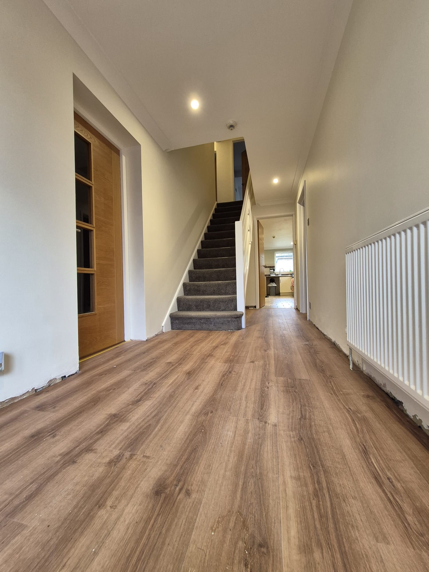 Long hallway in white with an oak door and stairs